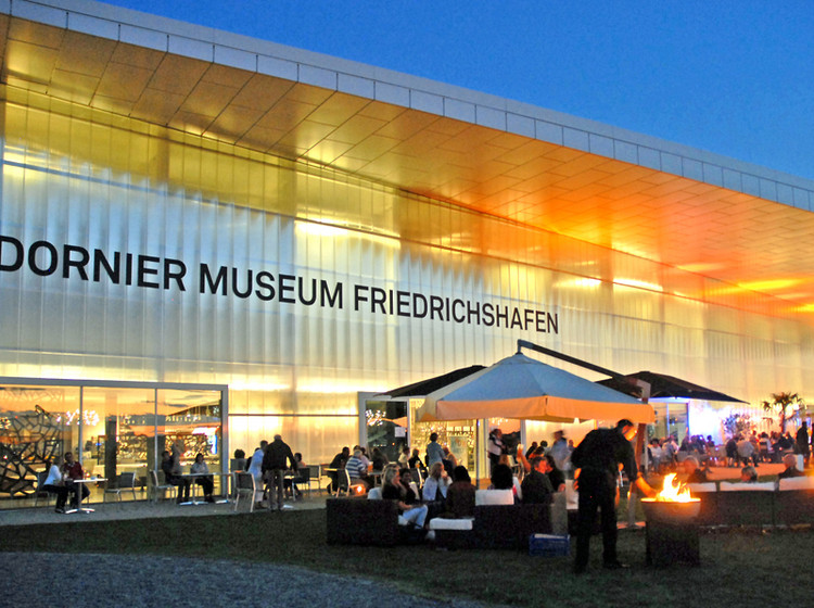 Grillfest am Abend im Außenbereich des Dornier-Museums, mit Tischen und Gästen unter stimmungsvoller Beleuchtung.