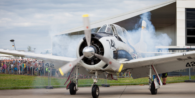 Ein Propellerflugzeug beschleunigt auf der Startbahn, dabei kommen Rauchschwaden aus den Triebwerken.
