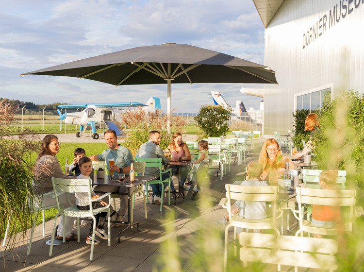 Mehrere Personen sitzen an den Tischen im Außenbereich des Dornier-Restaurants und genießen ihre Zeit.