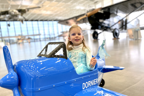 Verkleidetes Mädchen sitzt in einem blauen Spielzeugflugzeug.