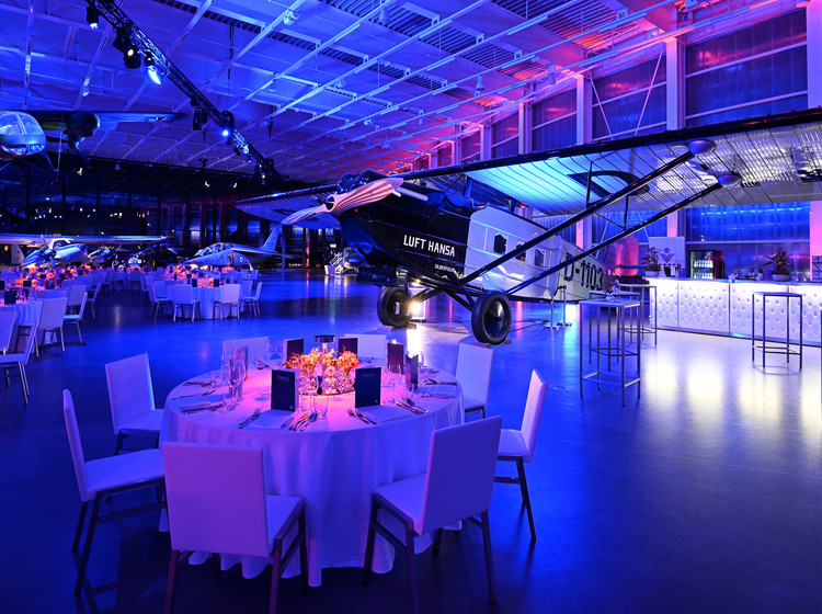 Gedeckte runde Tische für eine Gala im Hangar mit stimmungsvoller Beleuchtung.