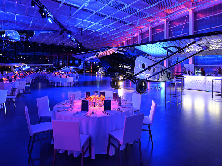 Gedeckte runde Tische für eine Gala im Hangar mit stimmungsvoller Beleuchtung.
