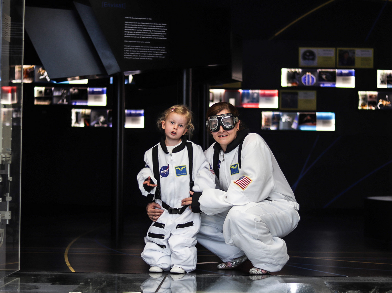 Mutter und Tochter erleben eine nächtliche Raumfahrtausstellung mit Astronautenanzügen.