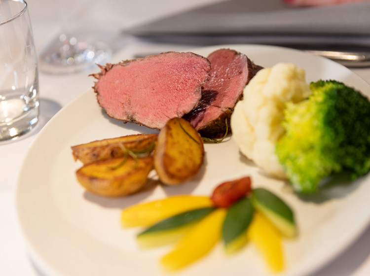 Tellergericht mit rosa gebratenem Rinderfilet, Brokkoli, Kartoffelspalten, Püree und dekorativ angerichtetem Gemüse auf weißem Teller.