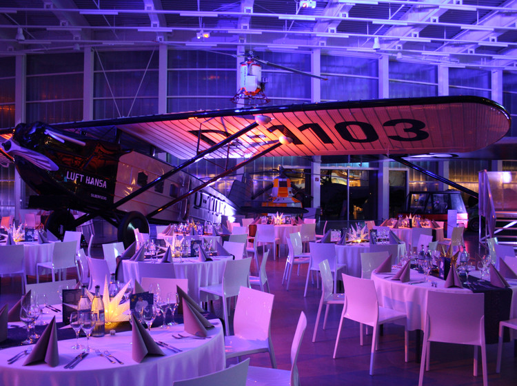 Tische und Stühle im beleuchteten Hangar Tische und Stühle sind im Hangar aufgestellt, der Raum ist stimmungsvoll beleuchtet.